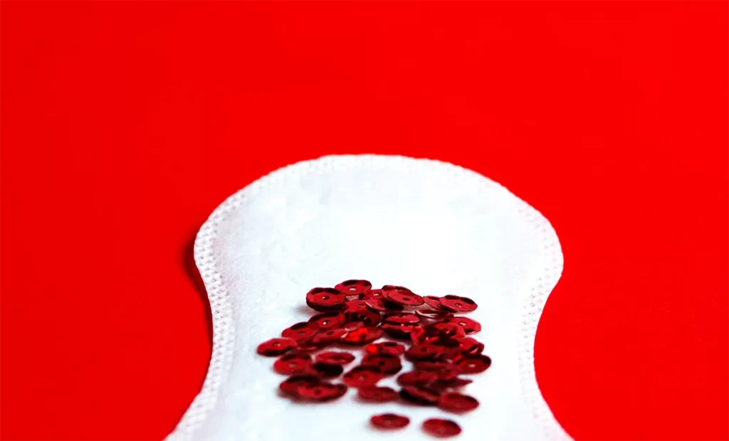 Imagen de una toalla íntima con algunas lentejuelas rojas, que simbolizan la sangre, utilizadas para calcular la fecha probable de parto. La toalla íntima se utiliza para medir la duración del ciclo menstrual y las lentejuelas rojas representan el día de inicio del periodo menstrual. Estos datos pueden ser utilizados junto con un calendario para estimar la fecha probable de parto